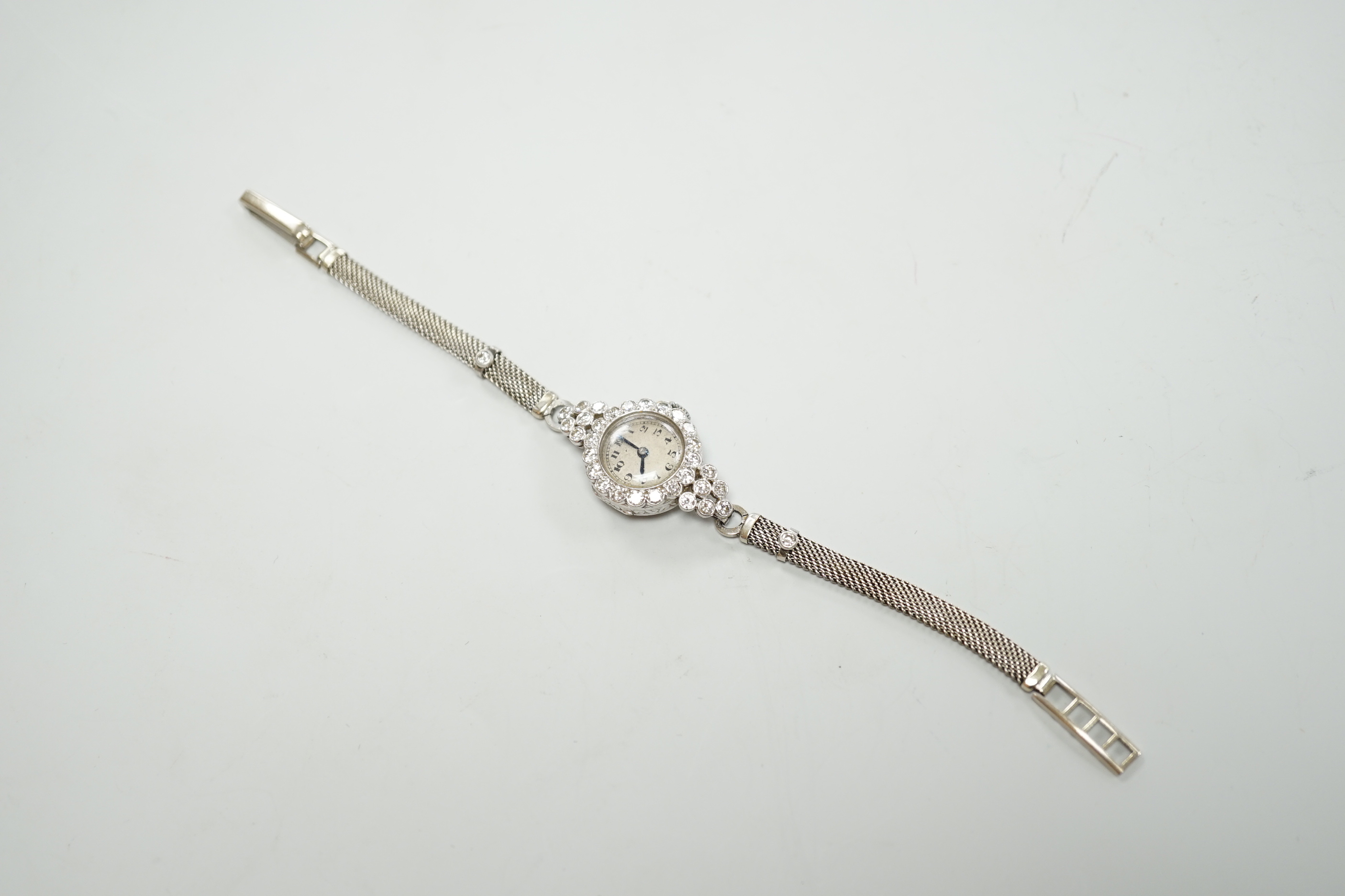 A lady's white metal and diamond set Movado manual wind cocktail watch, on a diamond set 9ct white metal mesh link bracelet, gross weight 18 grams.